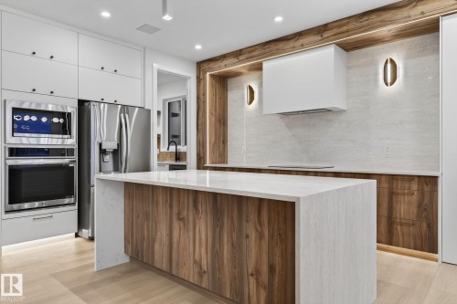Two tone kitchen with two tone cabinetry, stainless steel appliances, a center island, light stone countertops, and modern cabinets - 8765 Mayday Lane, Edmonton, AB - Indoor Photo Showing Kitchen