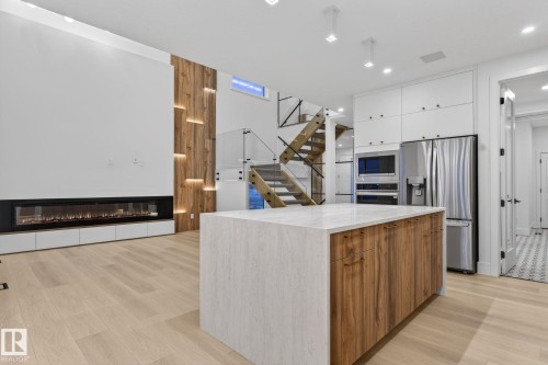 Two tone kitchen featuring modern cabinets, stainless steel appliances, a glass covered fireplace, two tone cabinetry, and light stone counters - 8765 Mayday Lane, Edmonton, AB - Indoor Photo Showing Kitchen