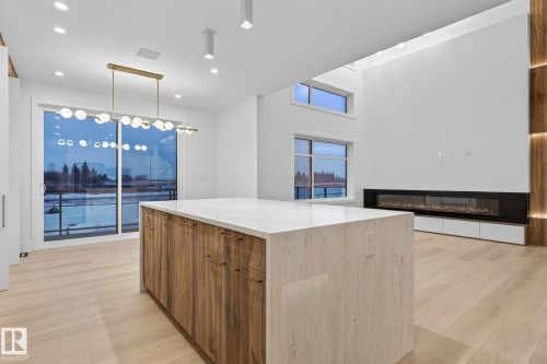 Kitchen featuring modern cabinets, a kitchen island, light stone counters, wood finish cabinets, and hanging light fixtures - 8765 Mayday Lane, Edmonton, AB - Indoor Photo Showing Kitchen