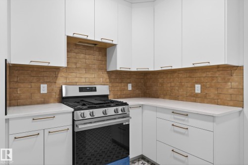 Kitchen with stainless steel range with gas stovetop, white cabinets, light stone countertops, and tasteful backsplash - 8765 Mayday Lane, Edmonton, AB - Indoor Photo Showing Kitchen