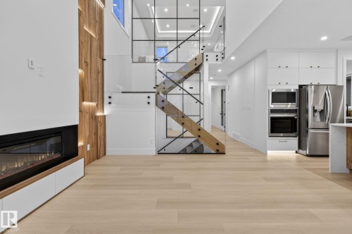 Unfurnished living room with a high ceiling, light wood-style floors, a glass covered fireplace, and recessed lighting - 8765 Mayday Lane, Edmonton, AB - Indoor With Fireplace