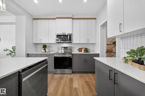 Dual tone kitchen featuring two tone cabinets, stainless steel appliances, light wood-style floors, light stone countertops, and tasteful backsplash - 20723 24 Avenue, Edmonton, AB - Indoor Photo Showing Kitchen With Upgraded Kitchen