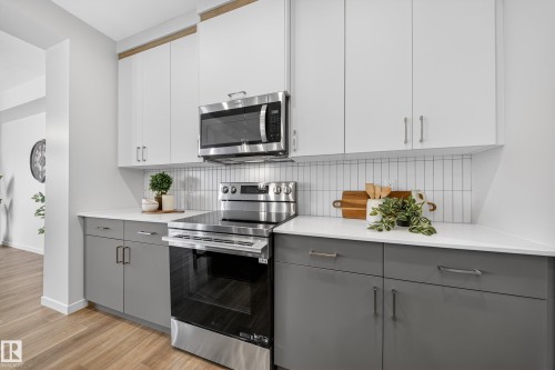 Two tone kitchen with dual tone cabinetry, stainless steel appliances, decorative backsplash, light wood-type flooring, and modern cabinets - 20723 24 Avenue, Edmonton, AB - Indoor Photo Showing Kitchen