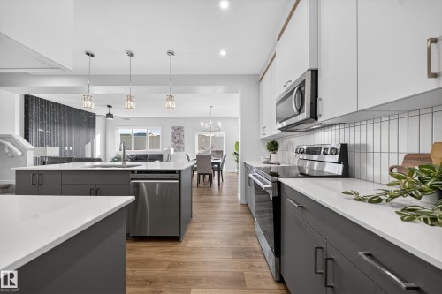 Two tone kitchen featuring stainless steel appliances, dual tone cabinetry, light wood-style floors, open floor plan, and suspended lighting - 20723 24 Avenue, Edmonton, AB - Indoor Photo Showing Kitchen With Upgraded Kitchen
