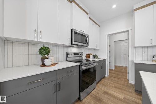 Dual tone kitchen with two tone color scheme, stainless steel appliances, light wood-style floors, tasteful backsplash, and light stone counters - 20723 24 Avenue, Edmonton, AB - Indoor Photo Showing Kitchen With Upgraded Kitchen