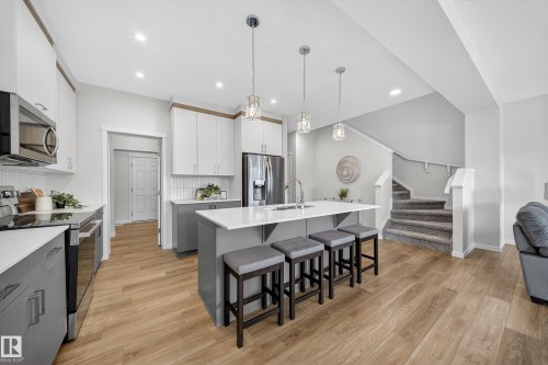 Kitchen with two tone color scheme, stainless steel appliances, a breakfast bar area, decorative light fixtures, and light wood-type flooring - 20723 24 Avenue, Edmonton, AB - Indoor Photo Showing Kitchen With Upgraded Kitchen