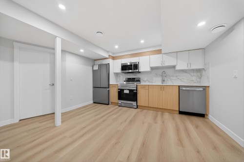 Kitchen with stainless steel appliances, dual tone cabinetry, light wood finished floors, tasteful backsplash, and light stone countertops - 20723 24 Avenue, Edmonton, AB - Indoor Photo Showing Kitchen