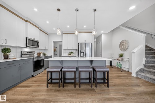 Two tone kitchen with dual tone cabinets, stainless steel appliances, a kitchen breakfast bar, decorative light fixtures, and light wood-style floors - 20723 24 Avenue, Edmonton, AB - Indoor Photo Showing Kitchen With Upgraded Kitchen
