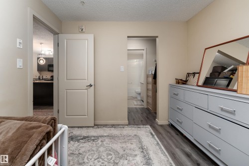 Bedroom with ensuite bathroom, a textured ceiling, and dark wood-style flooring - 205 340 Windermere Road, Edmonton, AB - Indoor