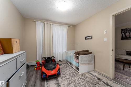 Bedroom featuring a crib, a textured ceiling, and dark wood-type flooring - 205 340 Windermere Road, Edmonton, AB - Indoor