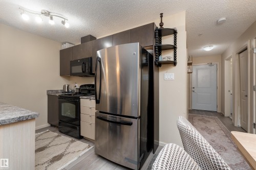 Kitchen with black appliances, light wood finished floors, a textured ceiling, light countertops, and dark wood finish cabinets - 205 340 Windermere Road, Edmonton, AB - Indoor Photo Showing Kitchen