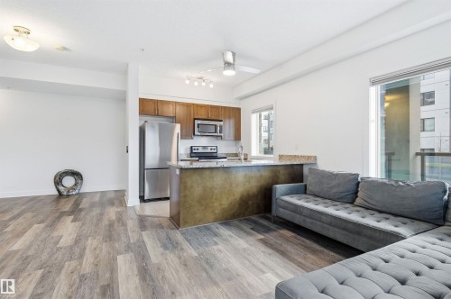 Kitchen with open floor plan, a peninsula, stainless steel appliances, light stone counters, and light wood-type flooring - 106 1238 Windermere Way, Edmonton, AB - Indoor