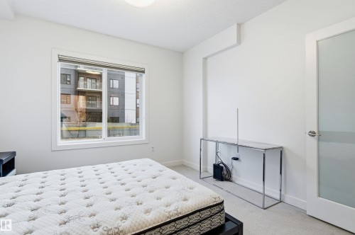 Bedroom with light colored carpet and baseboards - 106 1238 Windermere Way, Edmonton, AB - Indoor Photo Showing Bedroom