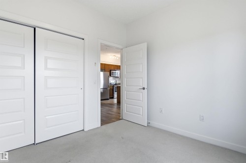Unfurnished bedroom featuring light colored carpet, a closet, and freestanding refrigerator - 106 1238 Windermere Way, Edmonton, AB - Indoor Photo Showing Other Room