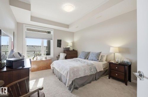 Bedroom with light carpet and a tray ceiling - 309 625 Leger Way, Edmonton, AB - Indoor Photo Showing Bedroom