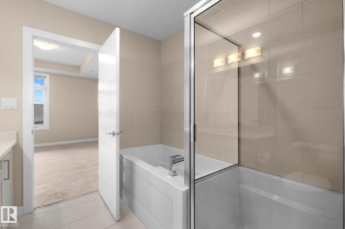 Bathroom featuring a built-in tub with a glass shower enclosure and tiled surround - 309 625 Leger Way, Edmonton, AB - Indoor Photo Showing Bathroom