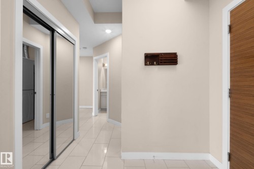 Hallway featuring light-toned tile flooring, neutral wall paint, and white baseboards - 309 625 Leger Way, Edmonton, AB - Indoor Photo Showing Other Room