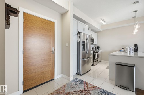Kitchen featuring stainless steel appliances, white cabinets, light stone countertops, light tile patterned floors, and track lighting - 309 625 Leger Way, Edmonton, AB - Indoor Photo Showing Kitchen