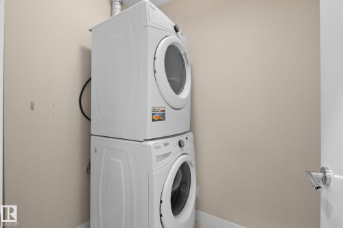 Dedicated laundry area featuring a stacked washer and dryer unit - 309 625 Leger Way, Edmonton, AB - Indoor Photo Showing Laundry Room