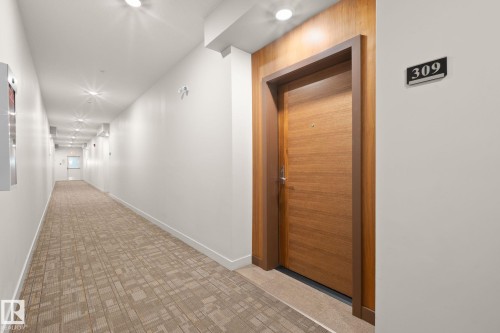 Warm wood-paneled entry door with modern hardware, framed by a contrasting brown trim - 309 625 Leger Way, Edmonton, AB - Indoor Photo Showing Other Room