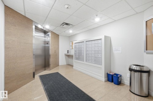 Elevator lobby featuring a stainless steel elevator, light-toned stone wall cladding, a drop ceiling with recessed lighting, and tile flooring - 309 625 Leger Way, Edmonton, AB - Indoor Photo Showing Other Room