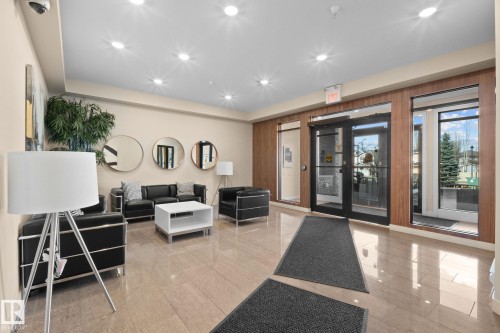 Lobby area featuring polished tile flooring, recessed lighting, wood-finish wall panels, and large glass entry doors - 309 625 Leger Way, Edmonton, AB - Indoor Photo Showing Other Room