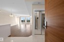 Entryway featuring wood-finish flooring, white tile, a contemporary pendant light fixture, and a built-in laundry area with stacked appliances behind mirrored closet doors - 309 625 Leger Way, Edmonton, AB  - Indoor Photo Showing Other Room 