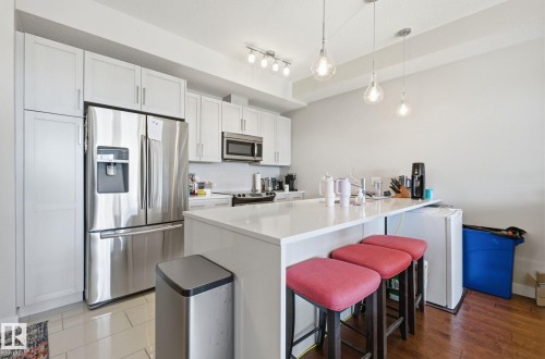 Kitchen with stainless steel appliances, a breakfast bar area, white cabinetry, decorative backsplash, and hanging light fixtures - 309 625 Leger Way, Edmonton, AB - Indoor Photo Showing Kitchen With Upgraded Kitchen