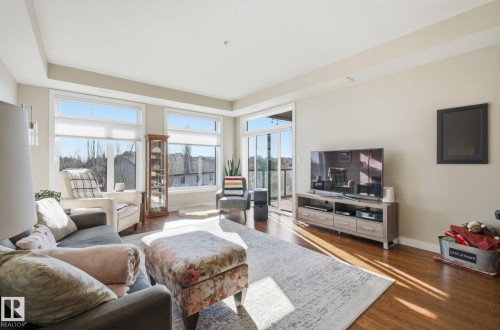Living room featuring dark wood finished floors and baseboards - 309 625 Leger Way, Edmonton, AB - Indoor Photo Showing Living Room