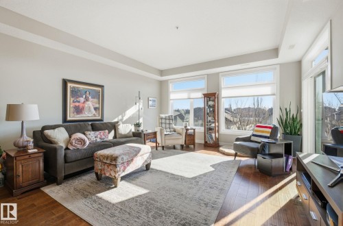 Living room featuring dark wood-style flooring and a tray ceiling - 309 625 Leger Way, Edmonton, AB - Indoor Photo Showing Living Room