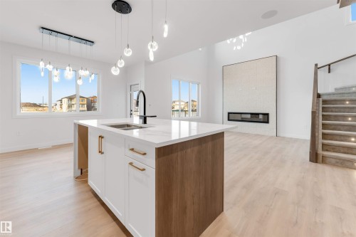 Kitchen with light wood-style flooring, light stone countertops, hanging light fixtures, open floor plan, and a center island with sink - 13 Trill Point(E), Spruce Grove, AB - Indoor Photo Showing Kitchen With Double Sink