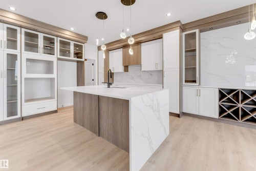 Kitchen featuring glass fronted cabinets, light stone countertops, dual tone cabinets, an island with sink, and light wood-style floors - 13 Trill Point(E), Spruce Grove, AB - Indoor Photo Showing Kitchen