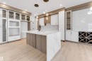 Kitchen featuring glass fronted cabinets, light stone countertops, dual tone cabinets, an island with sink, and light wood-style floors - 13 Trill Point(E), Spruce Grove, AB  - Indoor Photo Showing Kitchen 