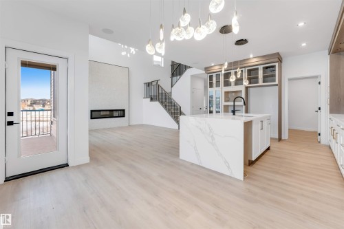 Kitchen with light stone counters, a kitchen island with sink, open floor plan, light wood-style floors, and a glass covered fireplace - 13 Trill Point(E), Spruce Grove, AB - Indoor Photo Showing Kitchen
