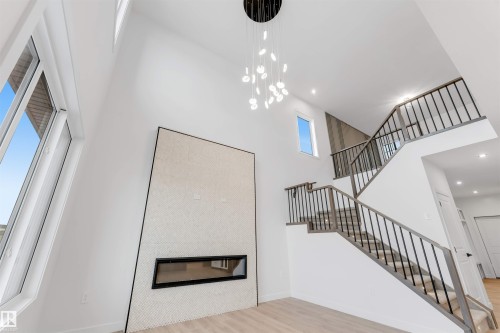 Unfurnished living room with light wood-style flooring, recessed lighting, a tiled fireplace, and a high ceiling - 13 Trill Point(E), Spruce Grove, AB - Indoor With Fireplace
