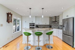 Kitchen with appliances with stainless steel finishes, pendant lighting, a kitchen breakfast bar, light stone counters, and wall chimney range hood - 