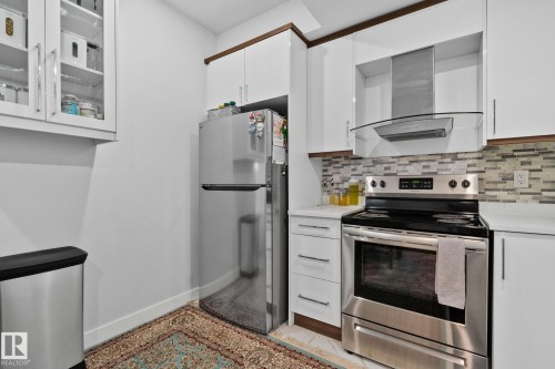 Kitchen featuring white cabinets, stainless steel appliances, glass insert cabinets, and backsplash - 1611 158 Street, Edmonton, AB - Indoor Photo Showing Kitchen