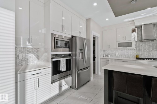 Kitchen featuring decorative backsplash, stainless steel appliances, light marble finish floors, modern cabinets, and light stone counters - 1611 158 Street, Edmonton, AB - Indoor Photo Showing Kitchen With Upgraded Kitchen