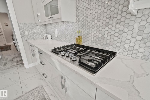 Kitchen view of stainless steel gas cooktop, light stone countertops, white cabinetry, and glass insert cabinets - 1611 158 Street, Edmonton, AB - Indoor Photo Showing Kitchen With Upgraded Kitchen