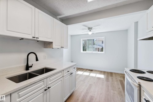 Kitchen featuring white cabinetry, electric stove, light wood-style floors, light stone counters, and a textured ceiling - 1096 Millbourne Road E, Edmonton, AB - Indoor Photo Showing Kitchen With Double Sink