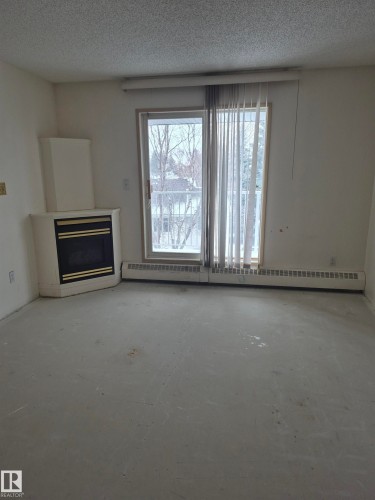 Unfurnished living room featuring a fireplace, a textured ceiling, and baseboard heating - 410 17467 98A Avenue, Edmonton, AB - Indoor With Fireplace