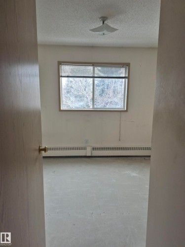 Unfurnished room featuring a textured ceiling, unfinished concrete flooring, and a baseboard radiator - 410 17467 98A Avenue, Edmonton, AB - Indoor Photo Showing Other Room