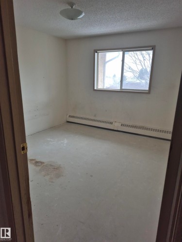 Empty room with unfinished concrete flooring, a baseboard heating unit, and a textured ceiling - 410 17467 98A Avenue, Edmonton, AB - Indoor Photo Showing Other Room