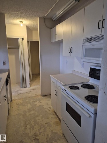 Kitchen with white appliances, a textured ceiling, light countertops, and white cabinets - 410 17467 98A Avenue, Edmonton, AB - Indoor Photo Showing Kitchen