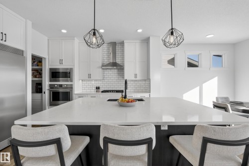 Kitchen featuring a breakfast bar, light stone countertops, built in appliances, backsplash, and hanging light fixtures - 9727 205 Street, Edmonton, AB - Indoor Photo Showing Kitchen With Upgraded Kitchen