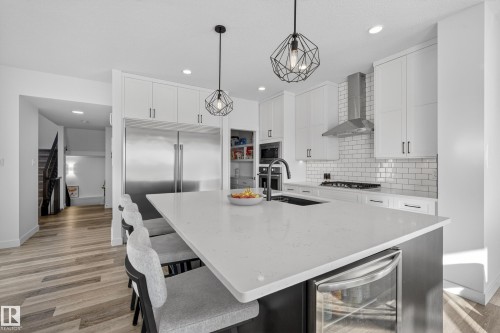 Kitchen featuring a center island with sink, light stone countertops, a breakfast bar area, wine cooler, and white cabinets - 9727 205 Street, Edmonton, AB - Indoor Photo Showing Kitchen With Upgraded Kitchen
