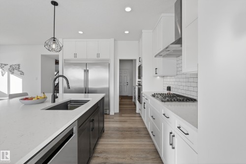 Kitchen featuring two tone cabinets, built in appliances, hanging light fixtures, light wood-style floors, and light stone counters - 9727 205 Street, Edmonton, AB - Indoor Photo Showing Kitchen With Double Sink With Upgraded Kitchen