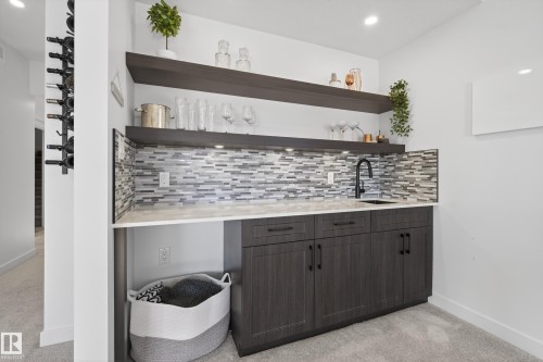 Indoor wet bar featuring light carpet, tasteful backsplash, dark wood finish cabinets, light stone counters, and open shelves - 9727 205 Street, Edmonton, AB - Indoor Photo Showing Other Room