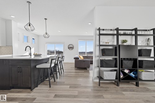 Kitchen featuring a breakfast bar, light wood-type flooring, light stone countertops, decorative light fixtures, and a peninsula - 9727 205 Street, Edmonton, AB - Indoor