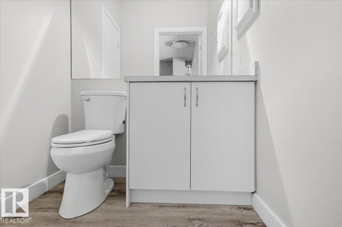 This bathroom features a contemporary vanity with a light-colored countertop, a modern toilet, and wood-look flooring - 6 6410 134 Avenue Nw, Edmonton, AB - Indoor Photo Showing Bathroom